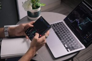 Trader checking stock charts on phone and laptop, reflecting market reaction to AI slowdown news