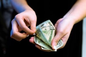 Hand holding US dollar bills, representing the Apple Siri settlement payout of up to $95 per device