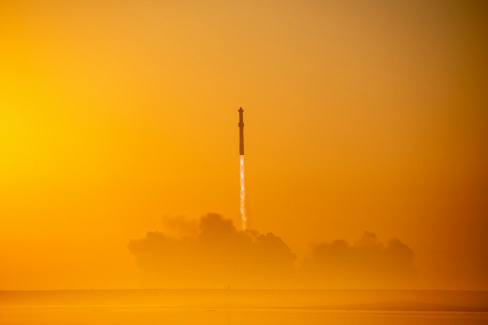 Starship rocket lifting off against an orange sky, with smoke clouds below