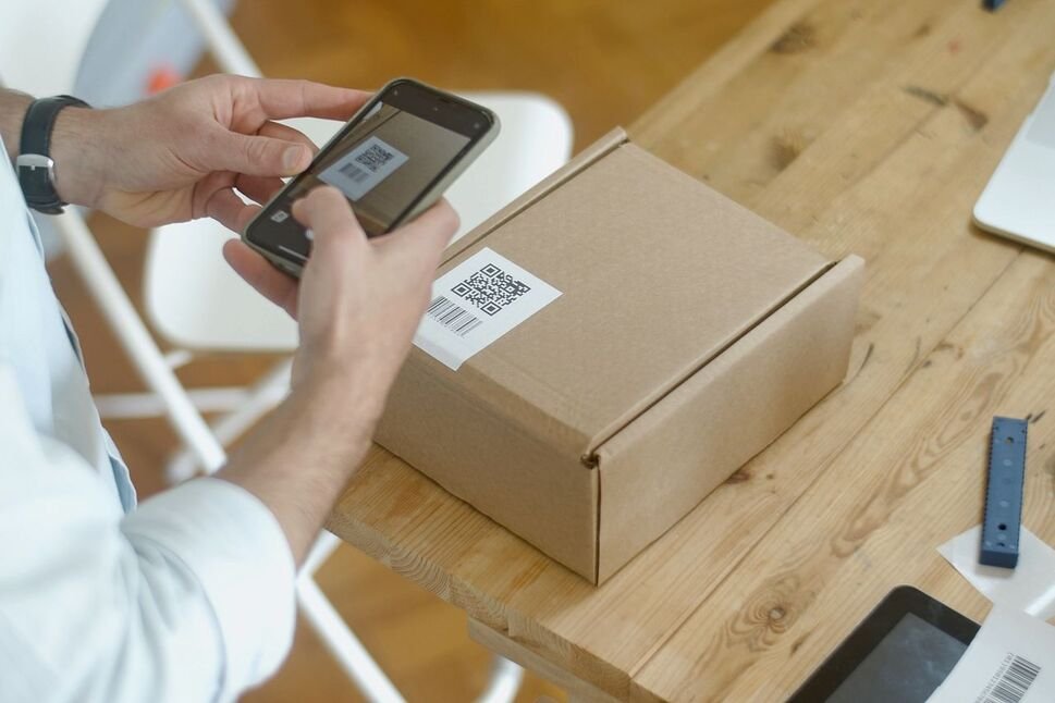 Man scanning a QR code on a parcel label with a smartphone, a common pretext in fake QR code delivery scams
