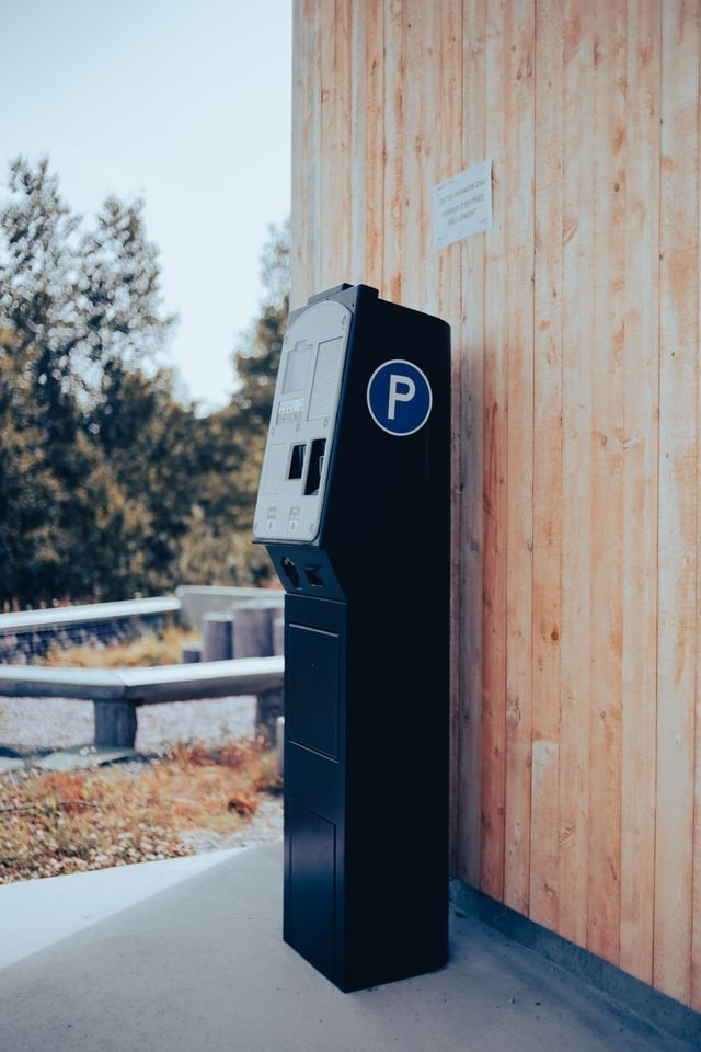 Street parking pay station beside a wooden wall, the kind of machine where scammers can stick a fake QR code over the real one